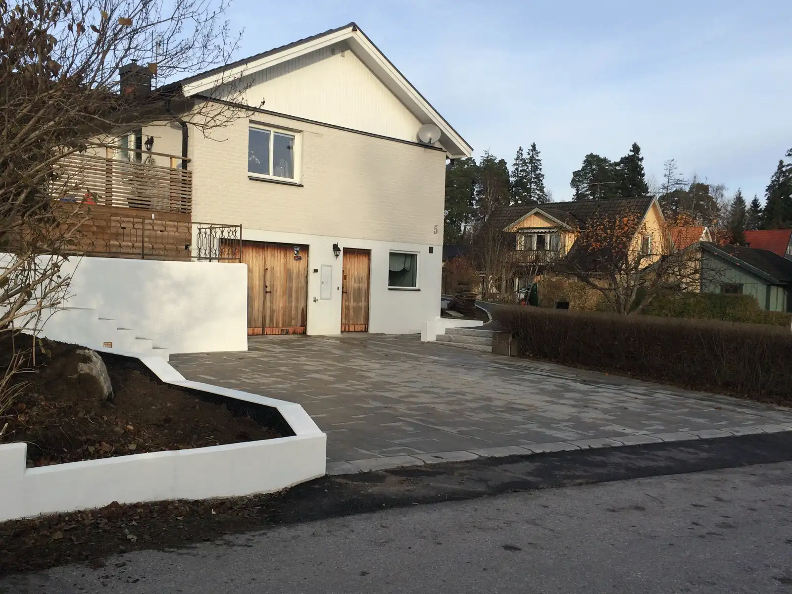 Bilden visar en snyggt anlagd uppfart som leder fram till ett modernt hus med en slät vit vägg som kantar vägen. Den naturliga stenläggningen skapar ett rent och elegant utseende, som kompletterar husets vita exteriör. Landskapsdesignen är minimal men effektiv, med en välskött häck och tydliga, definierade kanter, vilket ger en modern och inbjudande entré. Denna kombination av enkla, rena linjer och naturlig sten gör fastigheten både stilren och välkomnande. Bilden visar en snyggt anlagd uppfart som leder fram till ett modernt hus med en slät vit vägg som kantar vägen. Den naturliga stenläggningen skapar ett rent och elegant utseende, som kompletterar husets vita exteriör. Landskapsdesignen är minimal men effektiv, med en välskött häck och tydliga, definierade kanter, vilket ger en modern och inbjudande entré. Denna kombination av enkla, rena linjer och naturlig sten gör fastigheten både stilren och välkomnande.
